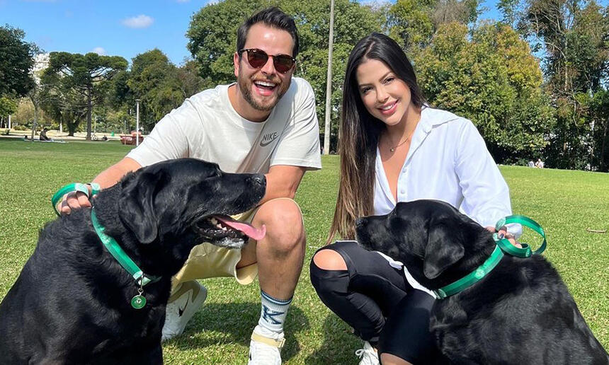 Gustavo e Lais de camisa branca, abaixados, sorrindo, ao lado dos cachorros