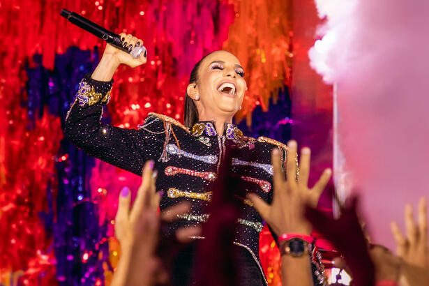 Ivete Sangalo com colete personalizado, segurando o microfone com a boca aberta, durante show para seu ep de carnaval