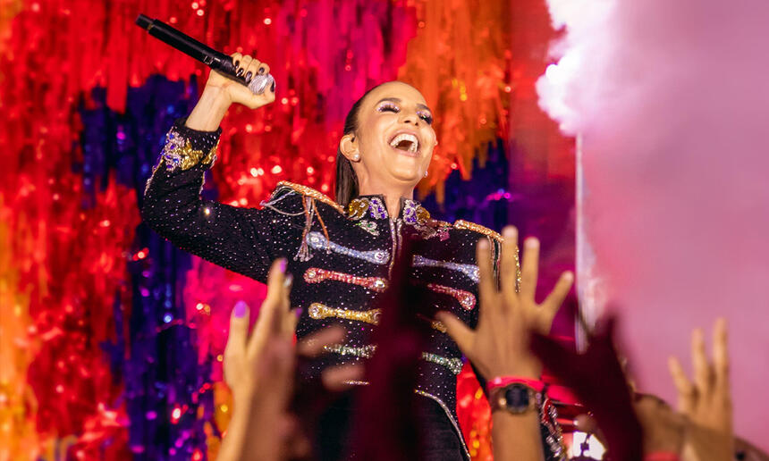 Ivete Sangalo com colete personalizado, segurando o microfone com a boca aberta, durante show para seu ep de carnaval