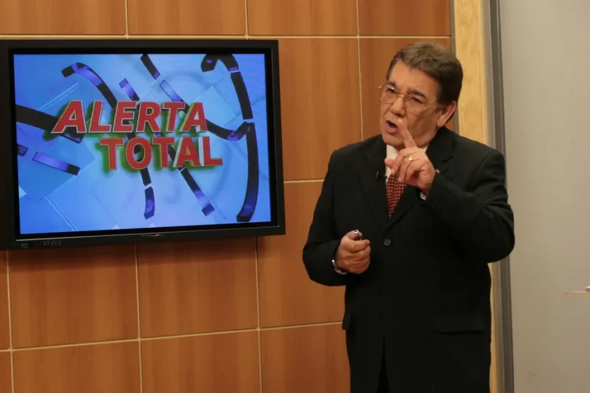 João Leite Neto de paletó preto, gravata e camisa social, de oculos, apontando pro câmera durante apresentação do Cidade Alerta;