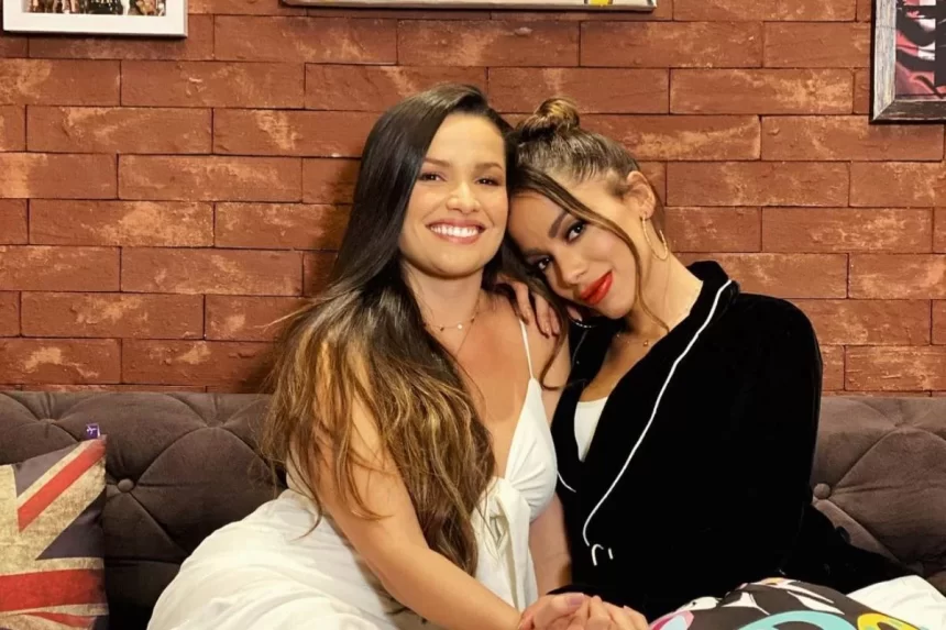 Juliette de vestido branco, sentada, sorrindo, ao lado de Anitta