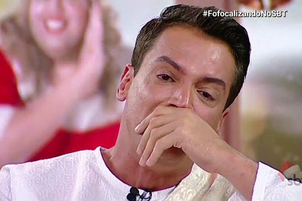 Leo Dias de camisa manga longa branca, com a mão na boca, chorando durante o Fofocalizando, do SBT