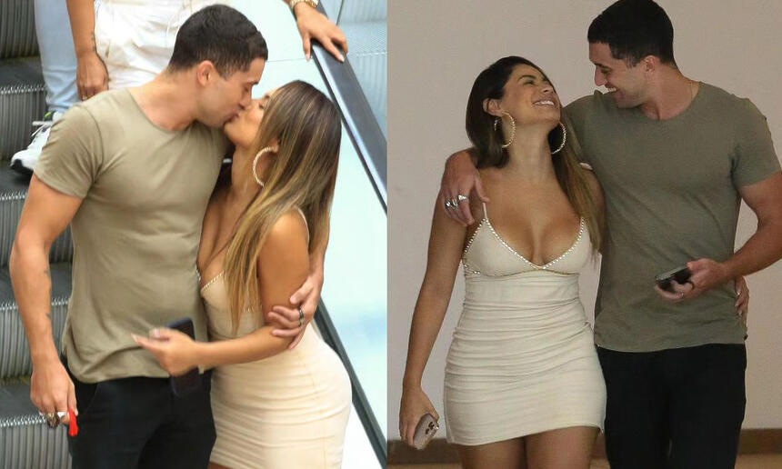 Lexa de vestido curto, bege, de cabelo solto, descendo a escada rolante abraçada com Ricardo Viana