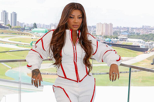 Ludmilla de look branco com detalhes vermelhos, cabelo solto, com semblante sério, encostada num ferro nos bastidores da GP SP 2024