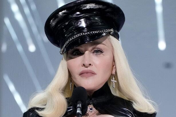 Madonna de cabelo loiro platinado, liso, usando um chapéu preto, com semblante sério, durante show da Celebration Tour