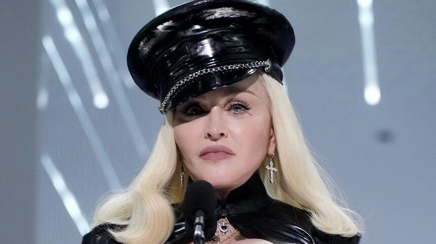 Madonna de cabelo loiro platinado, liso, usando um chapéu preto, com semblante sério, durante show da Celebration Tour