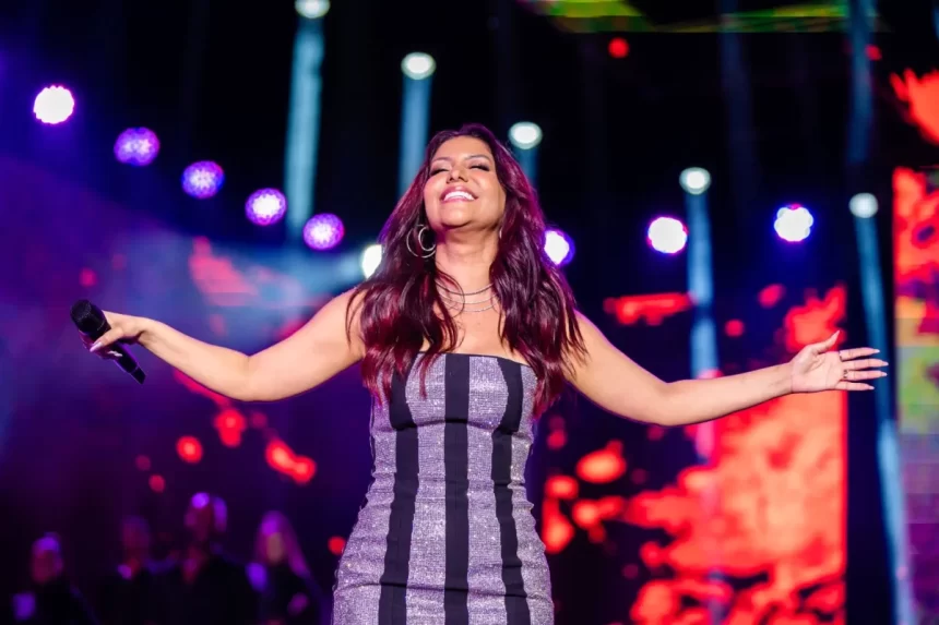 Priscila Senna sorrindo, com vestido prata e listra preta, com uma mulher no volante