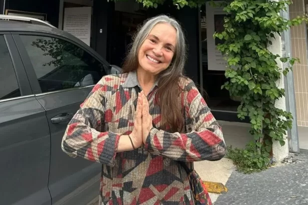 Regina Duarte sorrindo, com as mãos juntas, de camisa estampada em cores marrom, verde e magente