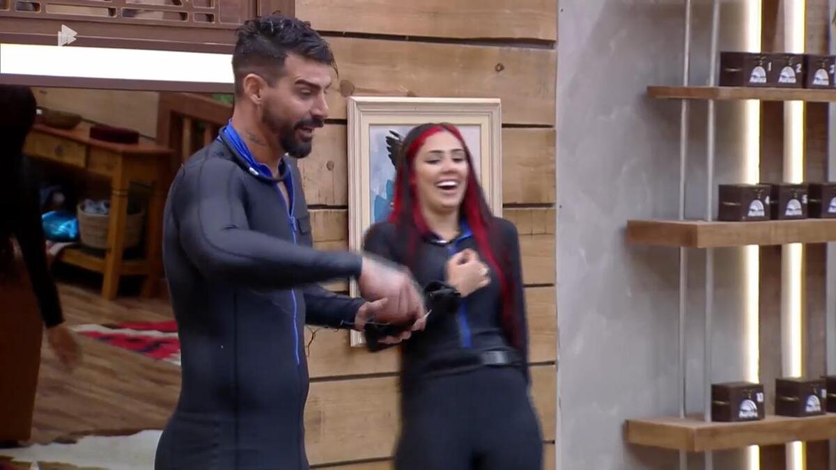 Alicia X sorrindo na sala de A Fazenda 15, enquanto Radamés explica Prova de Fogo