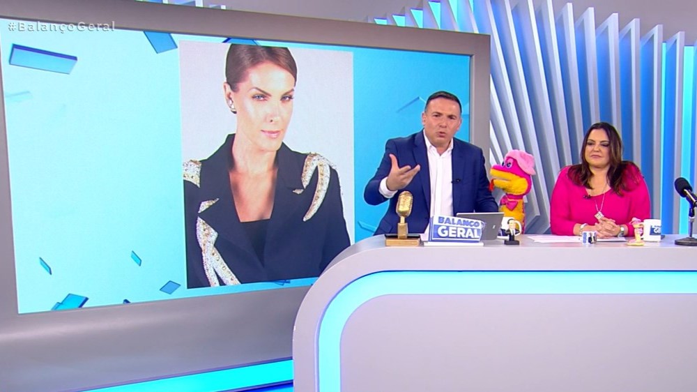 Ana Hickmann no telão do Balanço Geral e Reinaldo Gottino e Fabíola Reipert na bancada