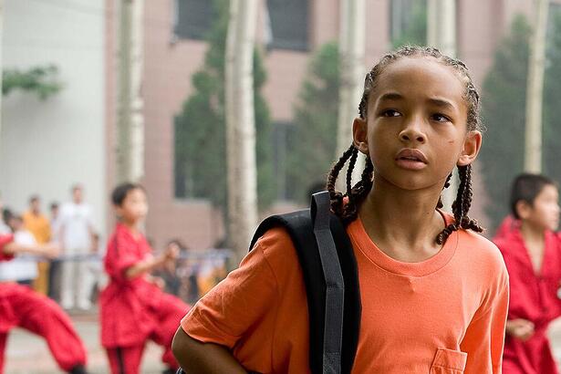 Jaden Smith em cena do filme Karated Kid. Ele veste uma camisa laranja e usa uma mochila nas costas