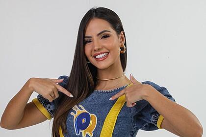 Luana Andrade aponta ao o logo do passa ou repassa, quadro do domingo legal, que está estampado na sua blusa