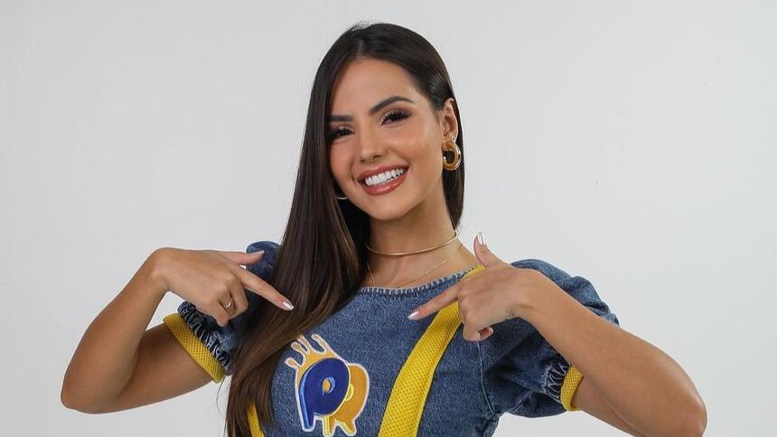 Luana Andrade aponta ao o logo do passa ou repassa, quadro do domingo legal, que está estampado na sua blusa