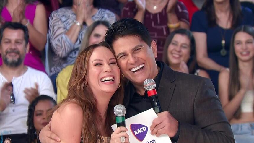 Regina Volpato abraça Cesar Filho. Os dois estão sorrindo no palco do Teleton 2023