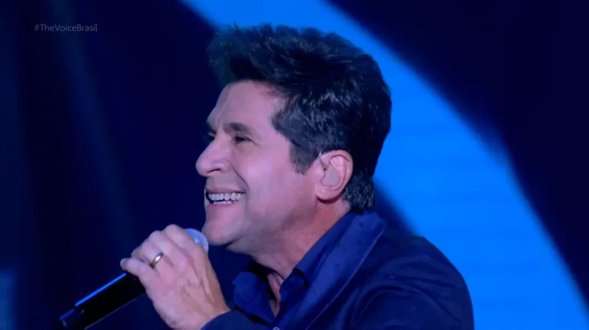 Daniel de blazer azul, de perfil, segurando microfone durante performance no The Voice Brasil