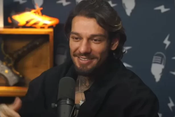 Lucas Lucco de perfil, sorrindo, em frente a um microfone, sentado durante entrevista em podcast