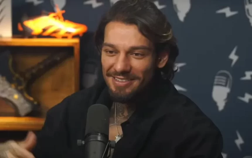 Lucas Lucco de perfil, sorrindo, em frente a um microfone, sentado durante entrevista em podcast