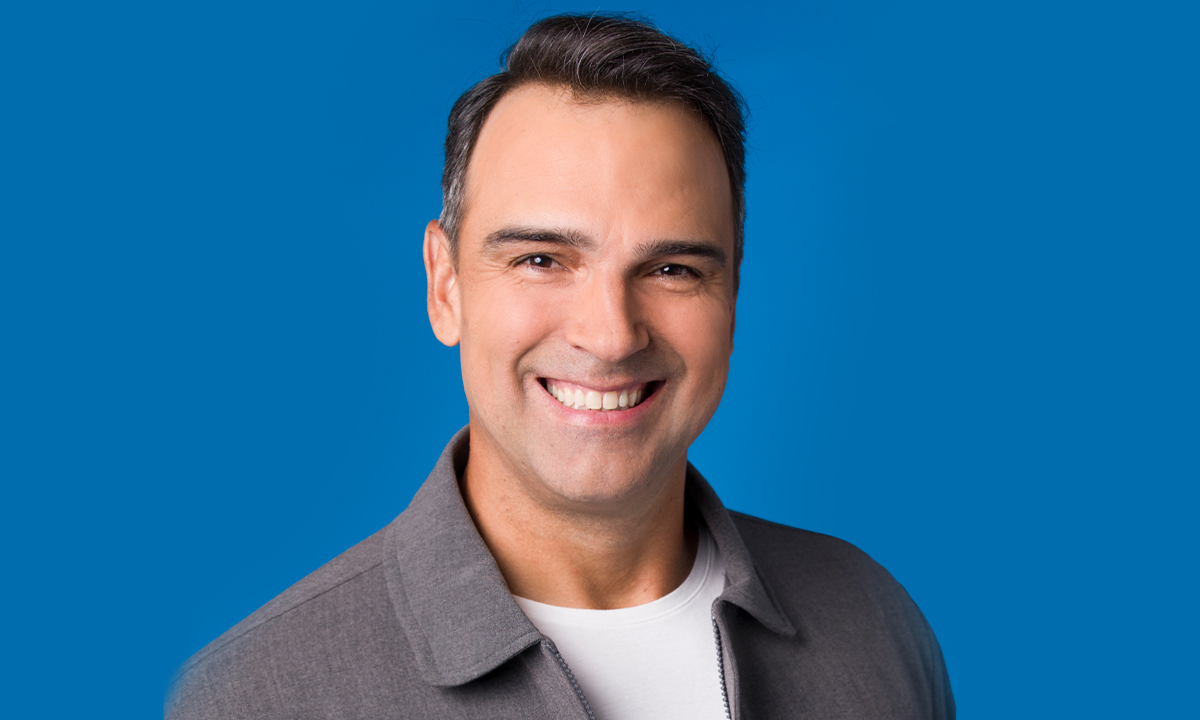 Tadeu Schmidt sorrindo de camisa branca e sobretudo cinza durante ensaio fotográfico do BBB 24