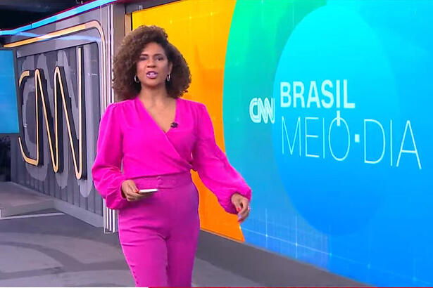 Luciana Barreto caminha próximo ao telão da CNN Brasil durante o telejornal Brasil Meio-Dia