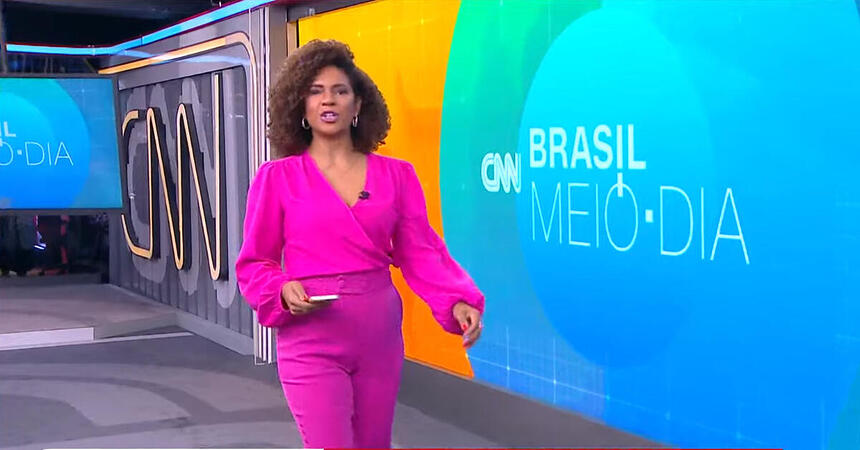 Luciana Barreto caminha próximo ao telão da CNN Brasil durante o telejornal Brasil Meio-Dia