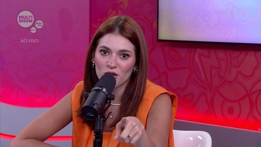 Ana Clara de vestido laranja, sentada, gravando mesacast do BBB 24