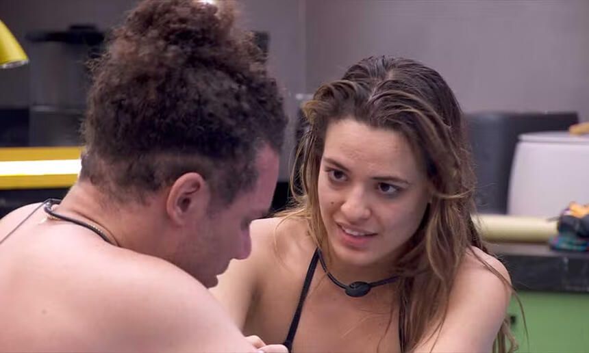 Beatriz de camisa molhado, biquini preto, sentada na mesa da Xepa