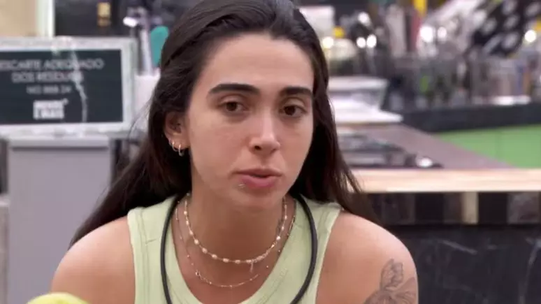 Giovanna de regata verde, cabelo preso, sentada na cozinha do BBB 24