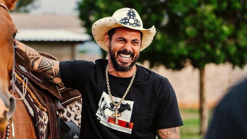 João Carreiro sorrindo ao lado de um cavalo. Ele será homenageado no Aparecida Sertaneja