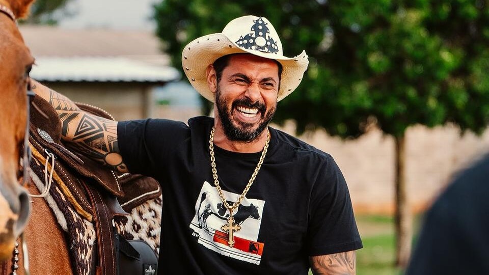 João Carreiro sorrindo ao lado de um cavalo. Ele será homenageado no Aparecida Sertaneja
