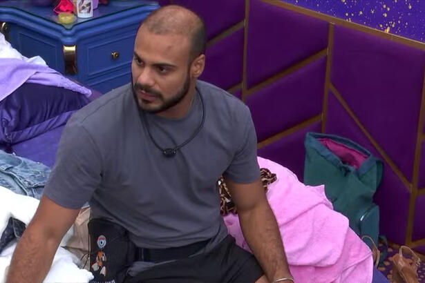 Marcus Vinicius de camisa cinza, sentado na cama do Quarto Magia do BBB 24