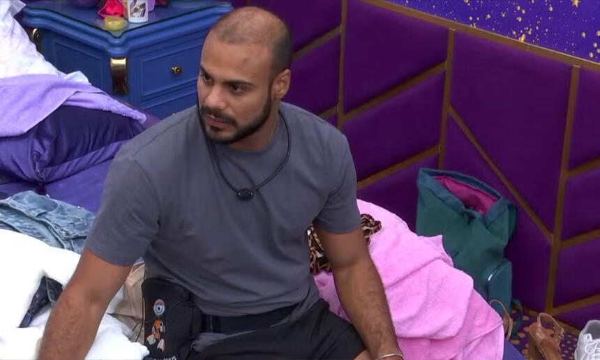 Marcus Vinicius de camisa cinza, sentado na cama do Quarto Magia do BBB 24