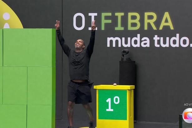 Rodriguinho de camisa e short preto, com as mãos levantas após vencer a prova do lider do BBB 24