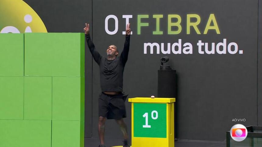 Rodriguinho de camisa e short preto, com as mãos levantas após vencer a prova do lider do BBB 24