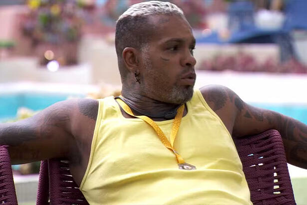 Rodriguinho de camisa regata amarela, com os braços abertos, sentado na varanda do BBB 24