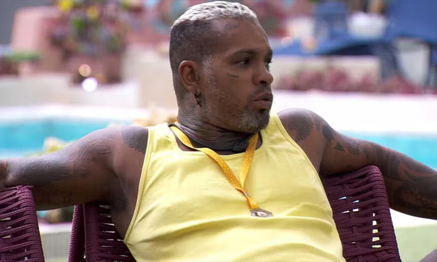 Rodriguinho de camisa regata amarela, com os braços abertos, sentado na varanda do BBB 24