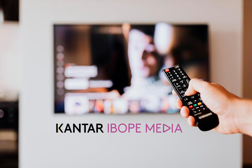 Pessoa pressionado o botão do controle remoto de uma TV e o logo da Kantar Ibope Media