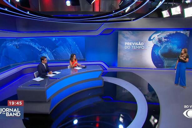 Rodolfo Schneider e Adriana Araújo sentados na bancada do Jornal da Band recebendo Joana Treptow na Previsão do Tempo