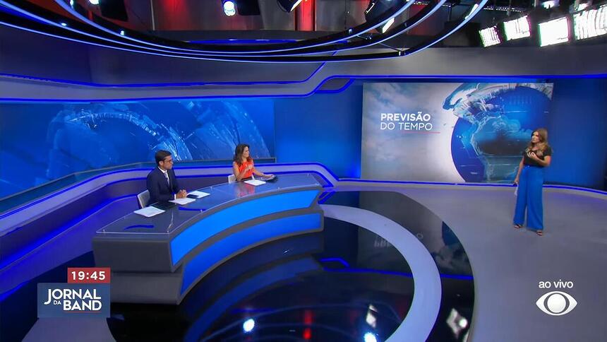 Rodolfo Schneider e Adriana Araújo sentados na bancada do Jornal da Band recebendo Joana Treptow na Previsão do Tempo