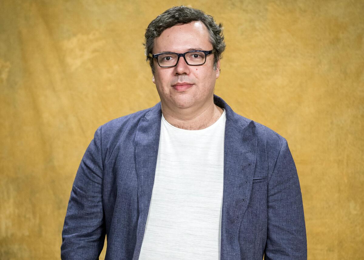 João Emanuel Carneiro em foto de divulgação com fundo amarelo