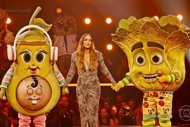 Ivete Sangalo segura a mão da Mamãe Abacate e Pé de Alface no cenário do The Masked Singer Brasil 4