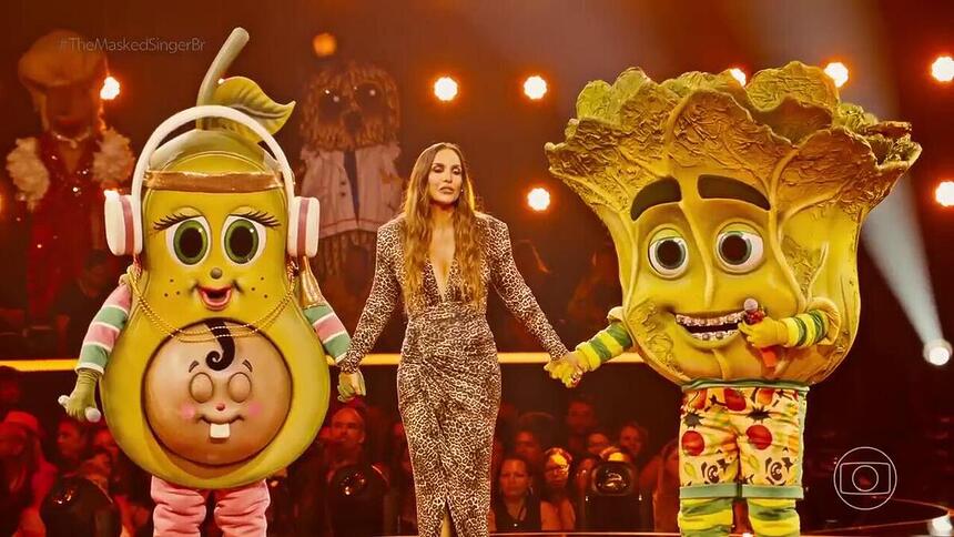 Ivete Sangalo segura a mão da Mamãe Abacate e Pé de Alface no cenário do The Masked Singer Brasil 4