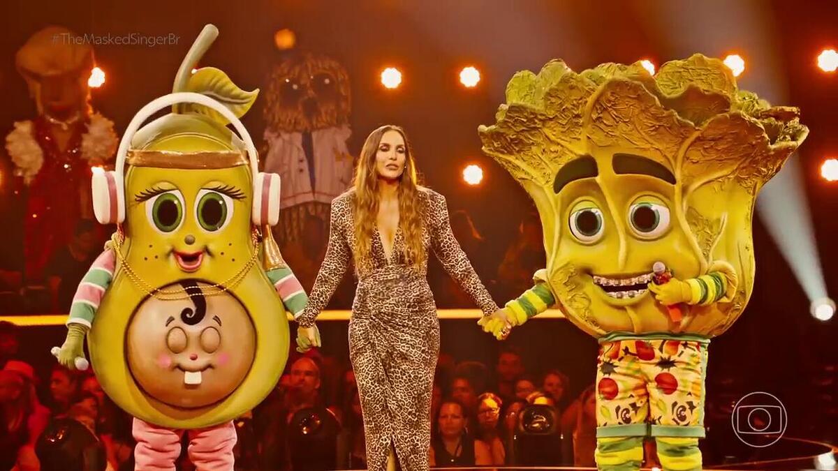 Ivete Sangalo segura a mão da Mamãe Abacate e Pé de Alface no cenário do The Masked Singer Brasil 4