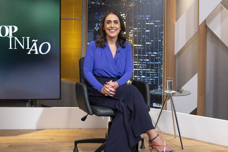 Rita Lisauskas sentada numa cadeira, sorrindo, no cenário do Opinião da TV Cultura