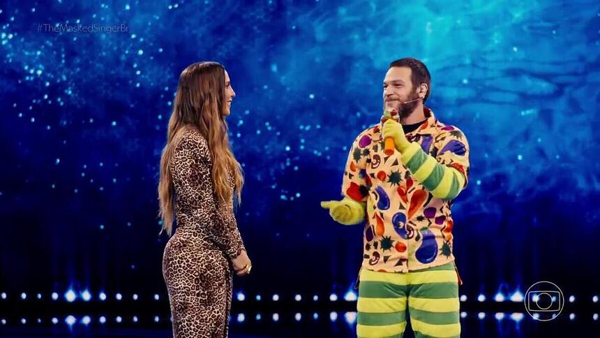 Ivete Sangalo e Emilio Dantas no palco do The Masked Singer Brasil. Emílio Dantas está com parte da fantasia de alface