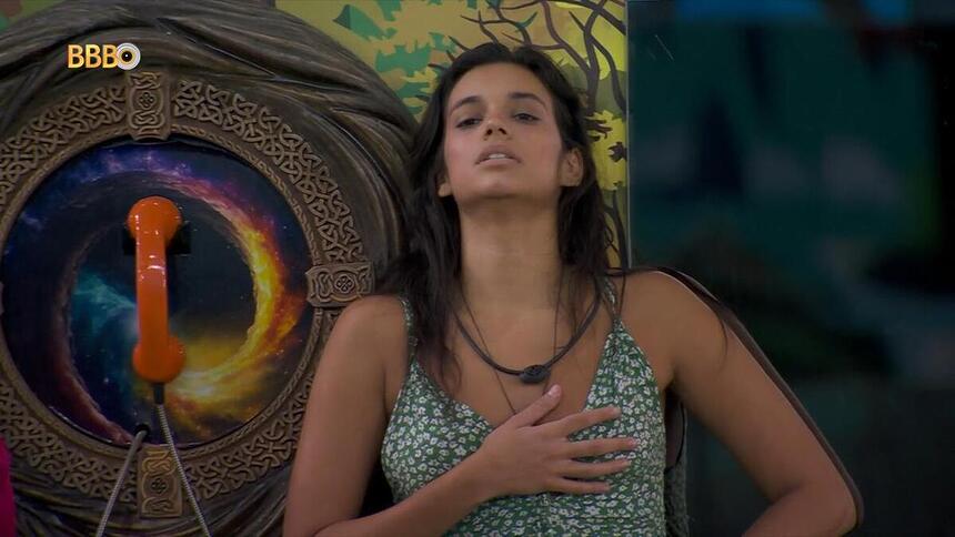 Alane com a mão no peito ao lado do Big Fone do BBB 24