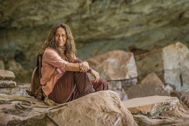 Andrea Beltrão é Zefa em No Rancho fundo. Ela está sentada numa grande pedra