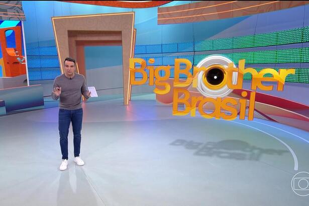 Tadeu Schmidt no centro do BBB 24, com as mãos levantadas, explicando a dinâmica da semana