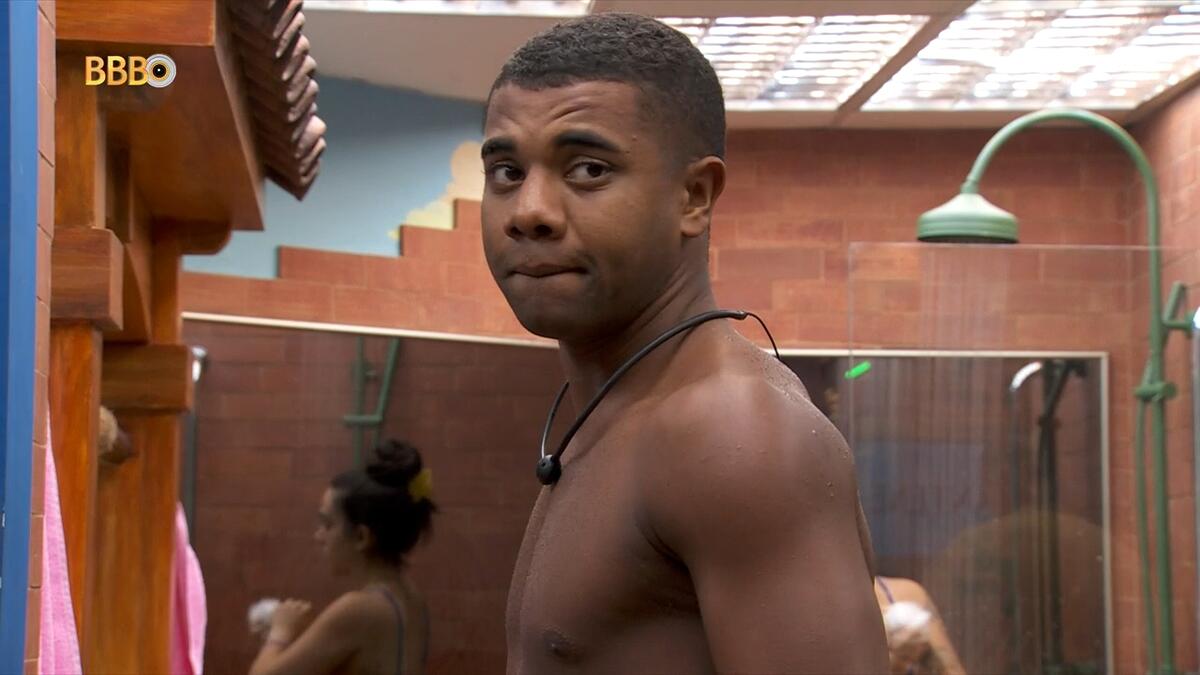 Davi, sem camisa, olhando para a câmera no banheiro