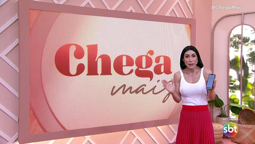 Michelle Barros com os braços abertos e segurando um celular em frente ao telão com o logo do Chega Mais