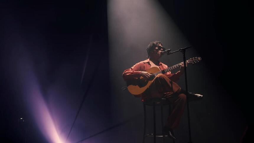 Djvan sentado, tocando violão, ao vivo em Maceió